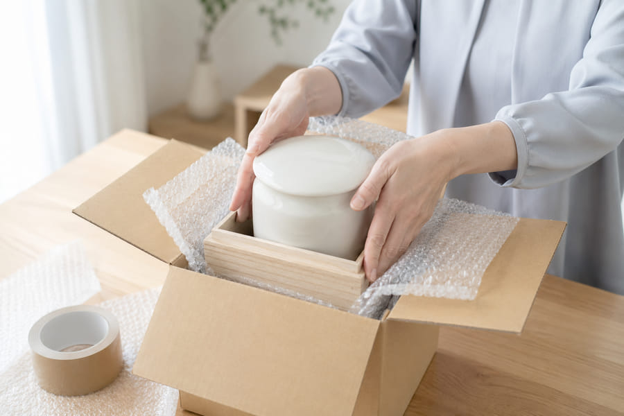 骨壺を桐箱に納め、緩衝材で包んで段ボール箱に梱包する様子