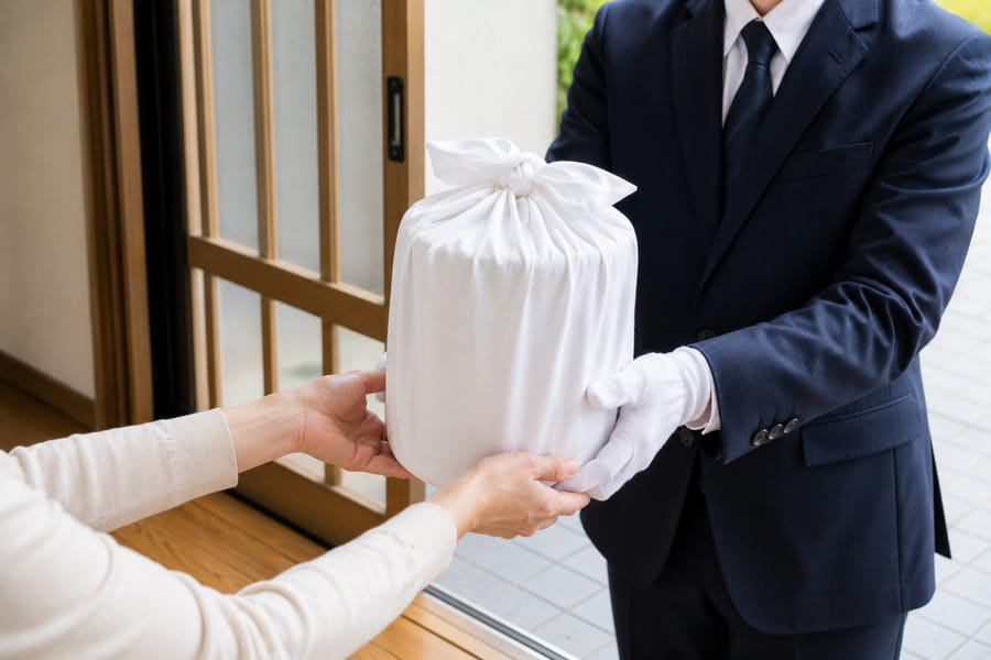 玄関先でスタッフが風呂敷に包んだ骨壺を受け取る様子